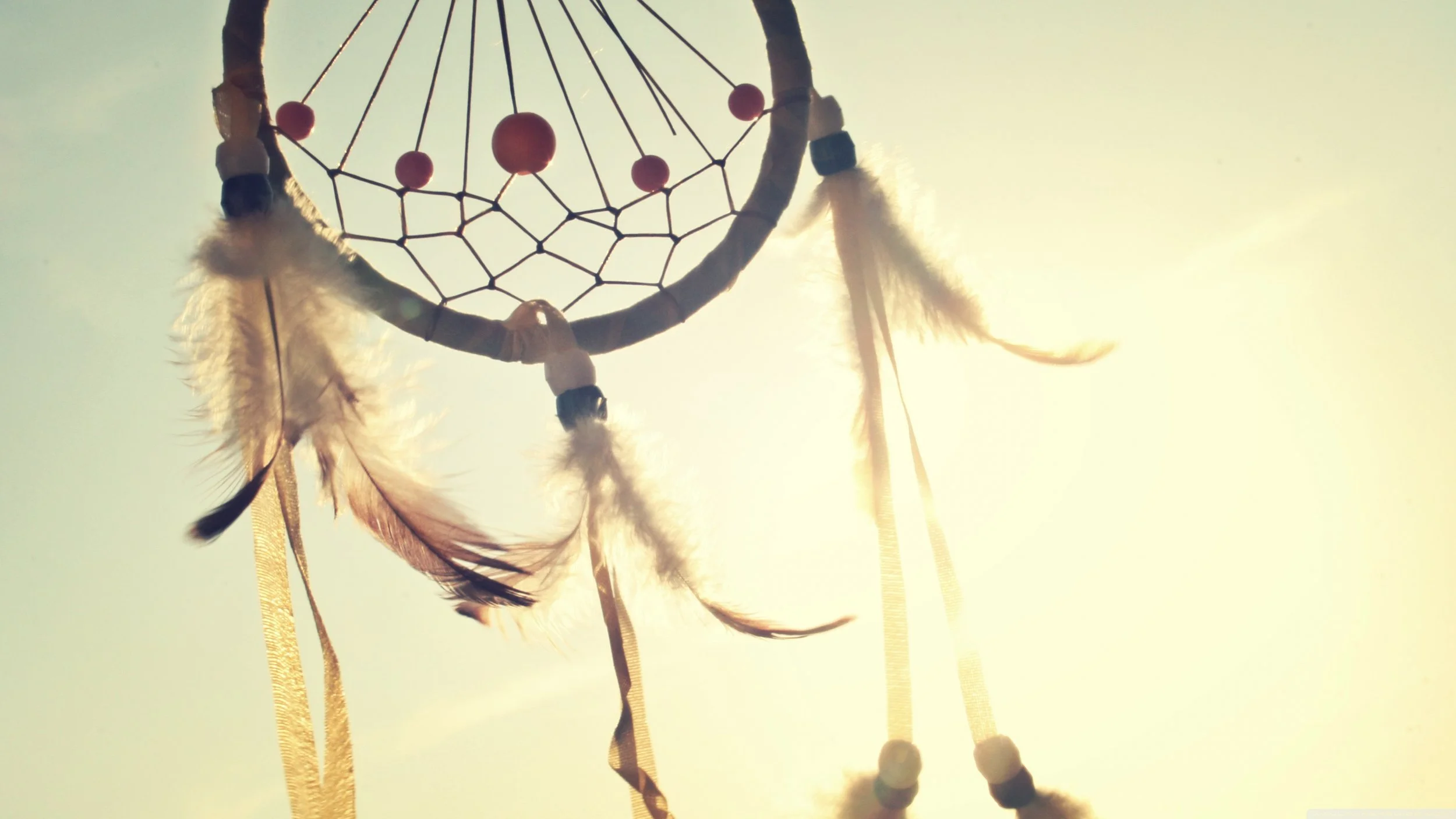 Dreamcatcher silhouette against a bright sunlit sky, warm golden tones, peaceful mood