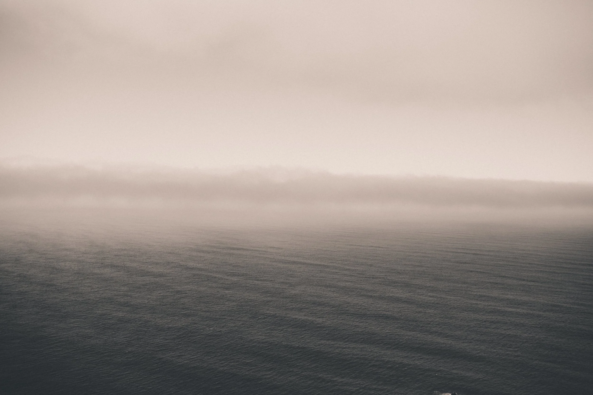 Foggy seascape with calm water and a low horizon, muted gray and pink tones, tranquil mood